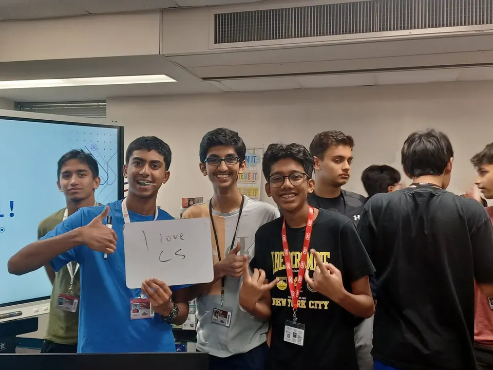 Members smiling and giving thumbs up behind an "I love CS" whiteboard sign.