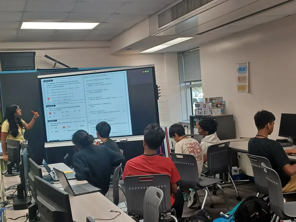 An officer points to a Java data-structures question on the classroom screen while members follow along.